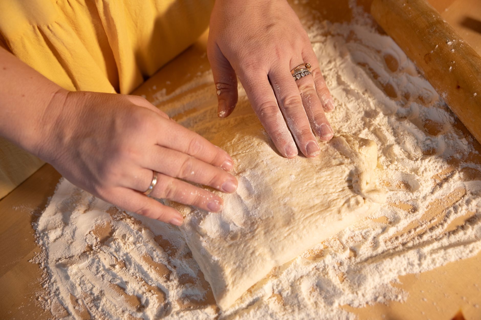 Close-up of hands kneading dough on a wooden surface with flour.
