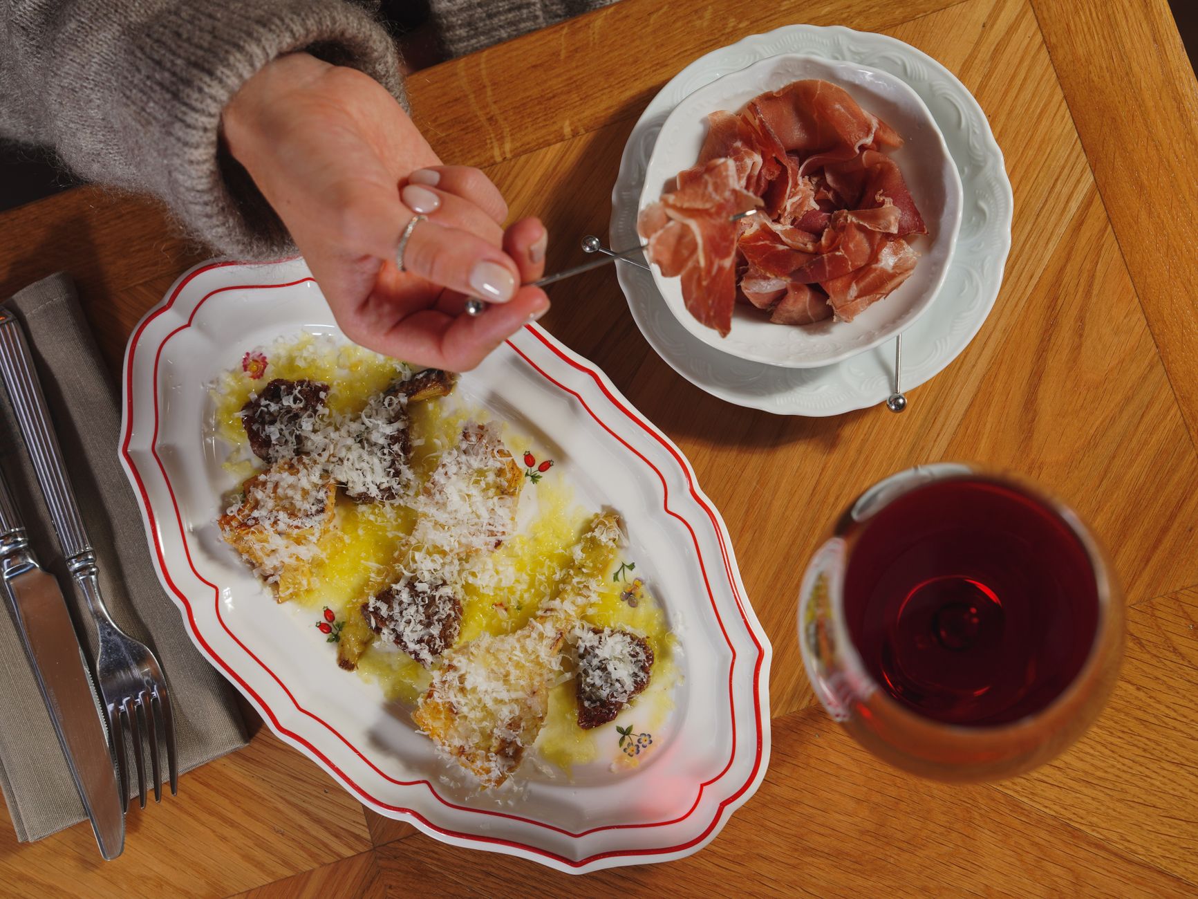 Savoring a gourmet meal with prosciutto and wine on a wooden table setting.