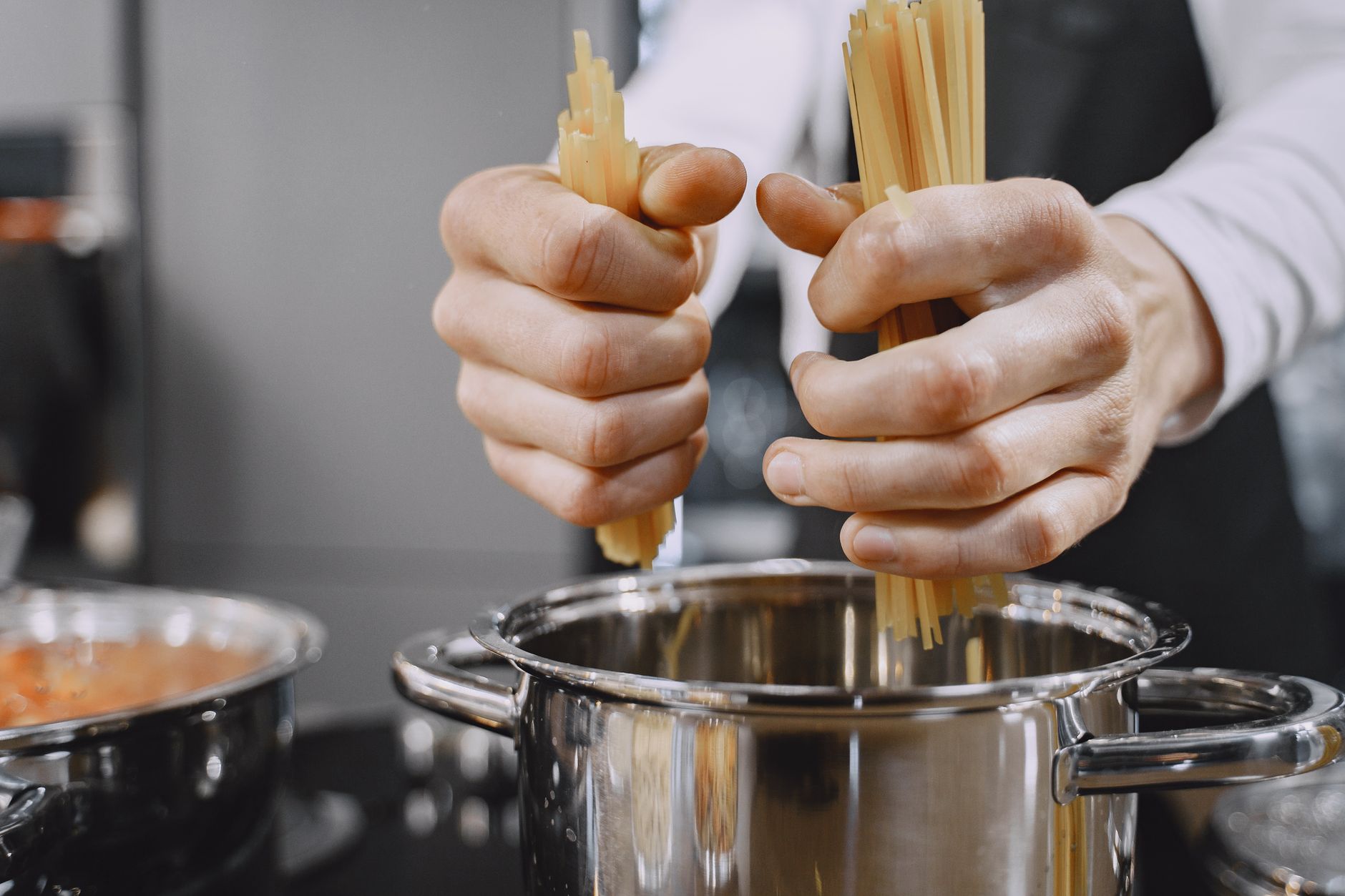 Close-up of chef's hands adding pasta to a boiling pot in a kitchen.