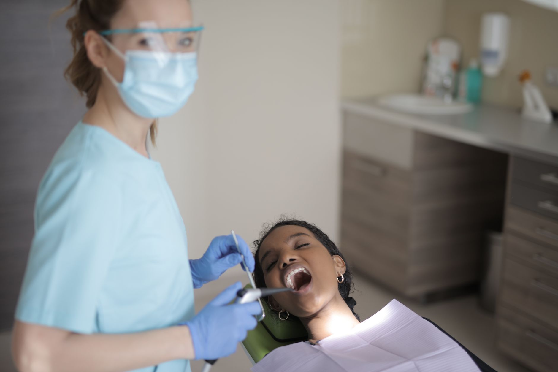Dentist in PPE gives a patient an oral checkup in a modern dental clinic setting.