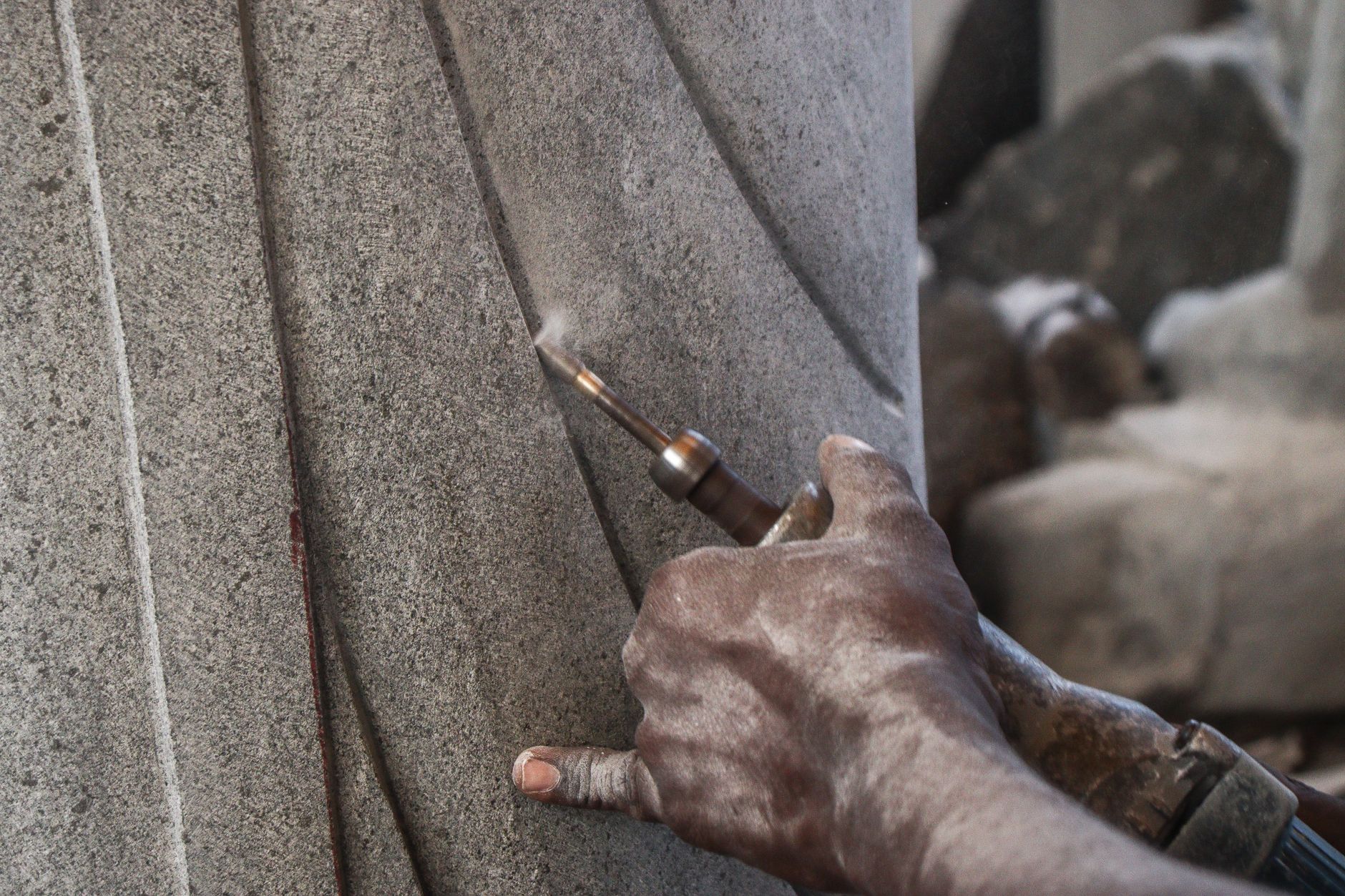 A close-up view capturing the hands of an artisan skillfully sculpting a stone column using a handheld tool.