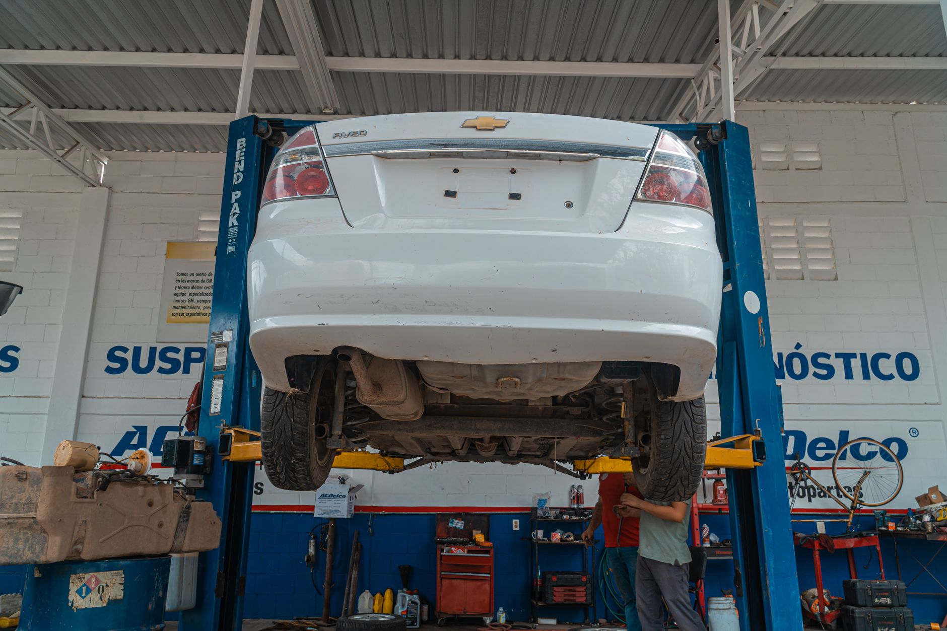 A white Chevrolet car is lifted for maintenance in an automotive repair shop.
